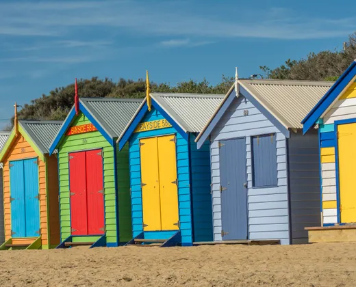 A row of brightly painted timber bathing boxes on a sandy beach under a clear sky