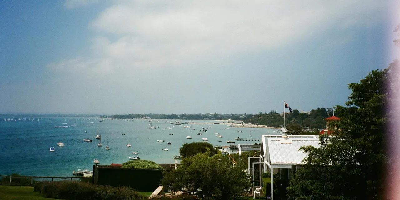 A quiet bay seen from a grassy slope, with small boats at anchor and houses along the shore