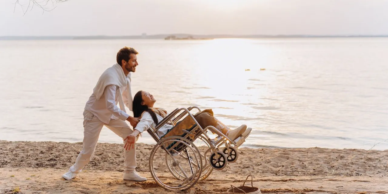 A woman using a wheelchair and a support worker together at the water's edge in low evening light